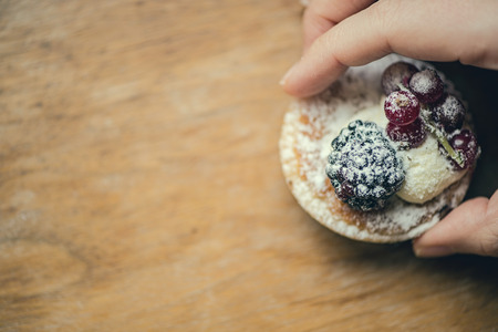 Pastry tarts with blackberries and red currants on a wooden board and in the woman handの写真素材
