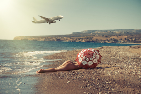Beautiful naked girl lying on the beach under an umbrella. Against the backdrop of the aircraftの写真素材