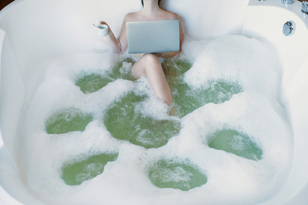 A girl in a hot tub in foam works at the computer and rests. The concept of lifestyleの写真素材