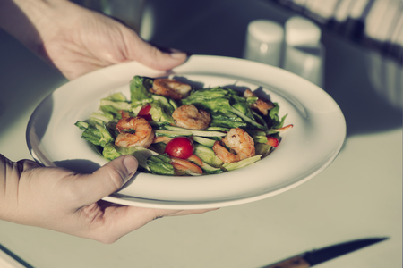 Female hands hold a plate with shrimp salad. The concept of eating and healthy lifestylesの写真素材