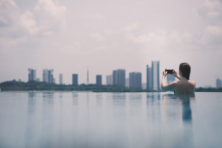 Beautiful girl in the pool with a mobile phone on the background of the city of Malaysia Putrajaya. Putrajaya Skyscrapersの写真素材