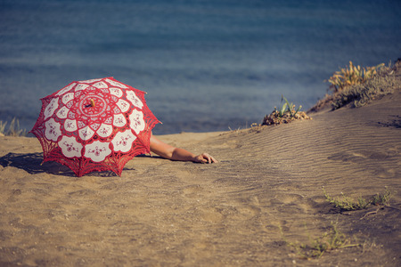 Beautiful naked female lies on the beach under a red umbrella. Girl on the sand under the umbrellaの写真素材