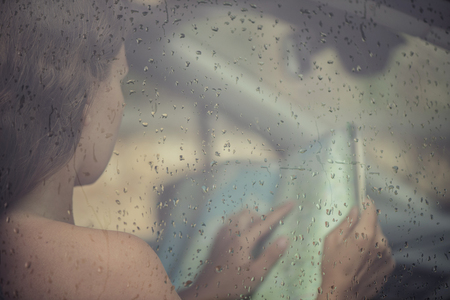 Woman looking in the map in the car window with rain drop. Young female behind rain car windowの写真素材