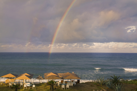 Rainbow over ocean and tropical beach with umbrellas chairs and tables. Top view.の写真素材