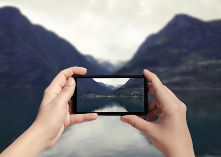 Picture of fjord in Norway on mobile phone. Female take picture of snow mountain on smart phone from...