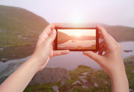 Picture of little lake on sunset in Norway on mobile phone. Female take photo of Suleskard on smart phoneの写真素材
