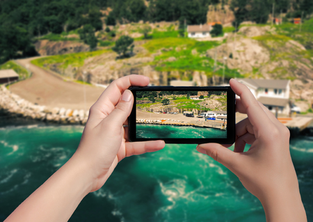 Picture of village Songesand in Norway on mobile phone. Female take picture houses and port in Lysefjorden on smart phoneの写真素材