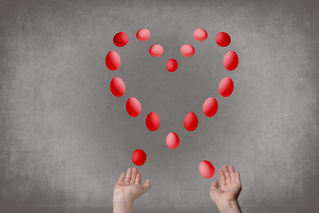 A female's hand juggles colorful eggs and they line up in shape of heart. Gray background.Concept of Easterの写真素材