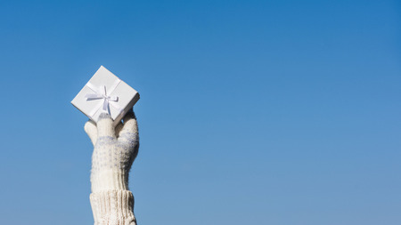 Woman hand in the knitted gloves with small white gift boxe. Winter and celebration concept.の写真素材