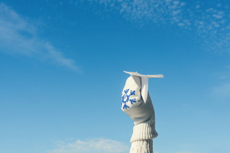 A girl in the winter knitted mittens is launching a paper airplane on the winter snowfall background. Christmas and New Year conceptの写真素材