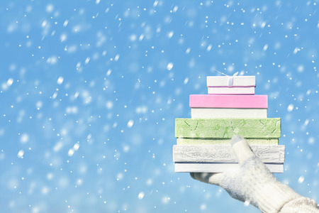 Woman hand in the knitted gloves with many gift boxes on the blue sky background. Concept of seasonal or winter discountの写真素材
