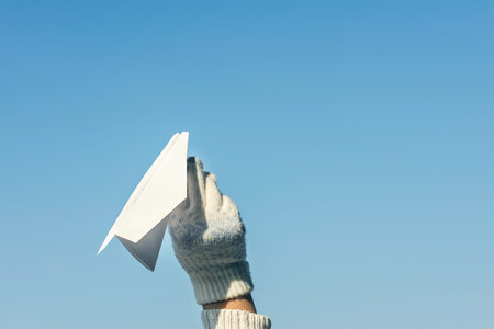 A girl in the winter knitted mittens is launching a paper airplane on the winter snowfall...