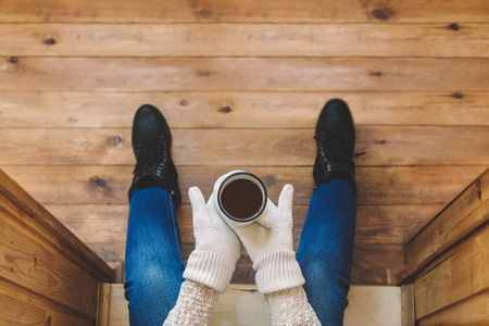 A girl in the boots with an iron mug of coffee on the terrace of a wooden house. Winter conceptの写真素材