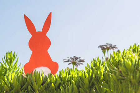 Creative easter concept photo of red paper rabbit in the chamomile flowers and green grass on the...