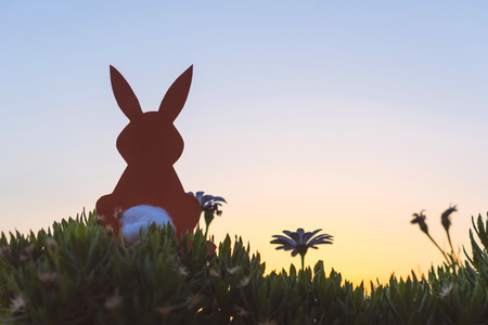 Creative easter photo of silhouette  paper rabbit in the chamomile flowers and green grass on the sunset sky background. Conceptの写真素材