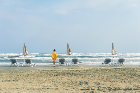 A boy in a yellow towel walks on the sandy Mackenzie beach in Larnaca in the autumn windy weather. Cyprusの写真素材