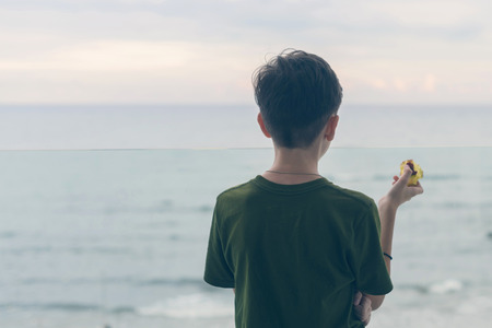 The boy is standing on the balcony eating an apple and looking at the seaの写真素材