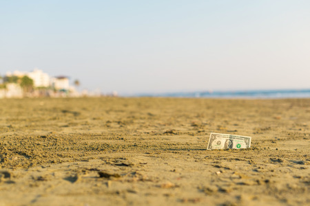 Banknote of value of one dollar in the the sand on the beach. Concept of cheap travel and vacation. Promotion and discountの写真素材