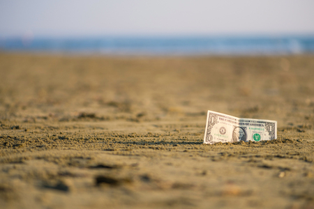 Banknote of value of one dollar in the the sand on the beach. Concept of cheap travel and vacation. Promotion and discountの写真素材