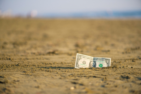 Banknote of value of one dollar in the the sand on the beach. Concept of cheap travel and vacation. Promotion and discountの写真素材