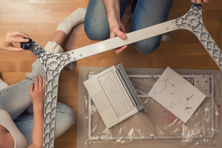 Man and woman assembling furniture  on wooden parquet using instruction for for self assembly