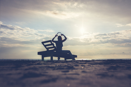 Girl in headphones is sitting on the sun lounger listening to music on the beach at sunset. Summer concept.の写真素材