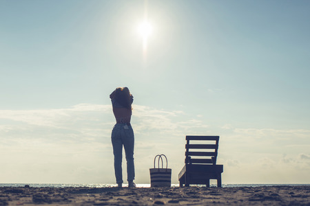 Woman standing near sun lounger and taking off her clother. Beach at sunset. Summer concept.の写真素材