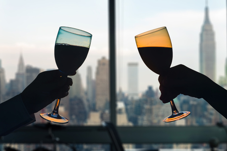 Man and female toasting with glasses of red wine in the apartment with New York city view.の写真素材