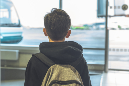 A boy with a backpack stands near glass door at the airport waiting transfer bus to the plane. Departure hallの写真素材