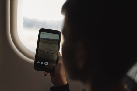 Caucasian boy using smartphone and taking picture during air flight.  Safety travel with kid. conceptの写真素材