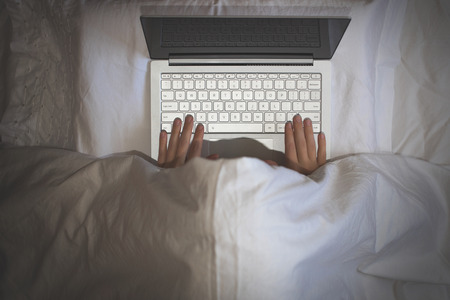 Girl lying with a laptop in bed covered by blanket. Woman can't sleep and have to work late at night. Top viewの写真素材
