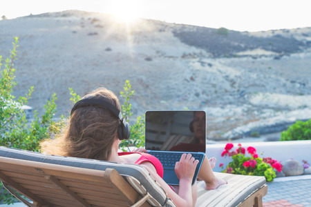 Woman freelancer with laptop in the swimsuit working on the lounger in her garden on the sunset.の写真素材