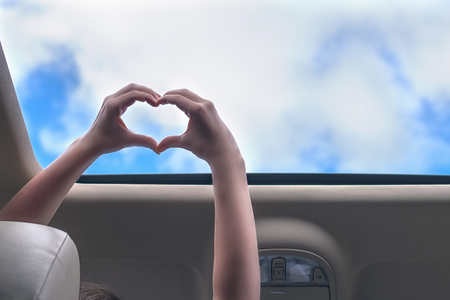 girl traveling by car and holds her hands in the form of heart out from open hatch of a vehicle. Travel lifestyle conceptの写真素材