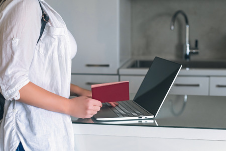 Online check in with laptop at home before travel. Female checking in to flight standing with pasport before traveling.の写真素材