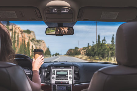 The girl is driving on the highway and holding paper cup of coffee . View from the back seat of the...