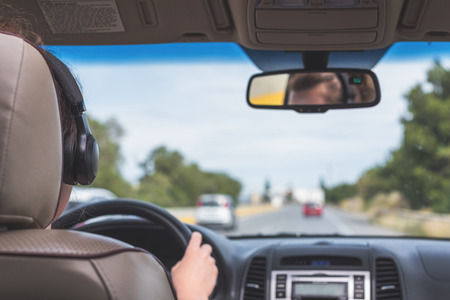 The girl in the headphones is driving on the highway in Italy. View from the back seat of the car on the windshield, road and the driverの写真素材