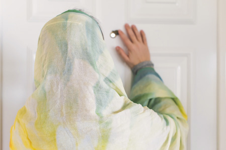muslim woman in a colorful scarf looking on peephole door when somebody rings the doorbellの写真素材