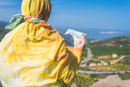 A lonely Muslim woman  traveler in a colorful scarf with map on top of a mountain.の写真素材