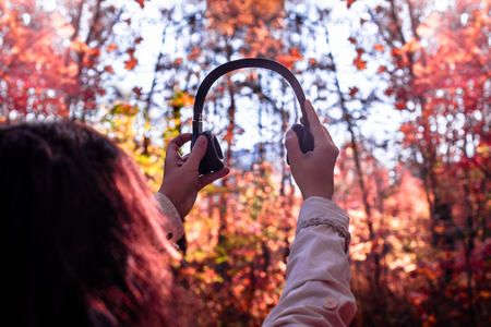 Female with headphones walking on the park listen sounds or music of autumn forest. Concept. Indian summer seasonの写真素材