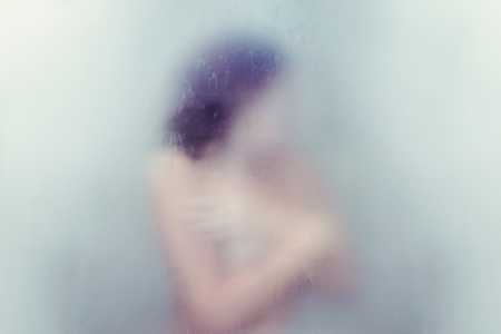 Silhouette of a lonely young woman hugging herself in the shower. Concept of depression and lonelinessの写真素材