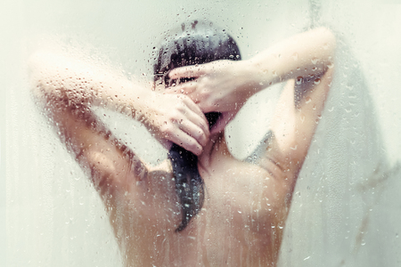 Silhouette of naked beautiful woman washing hair in shower behind wet misted glass.の写真素材