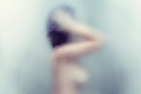 Naked beautiful woman taking a shower behind wet misted glass.の写真素材