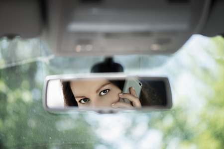 Reflection of young woman talking on a mobile phone in the car rear view mirror. No cell phone, while driving. Safe driving concept.の写真素材