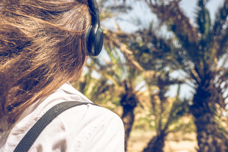 Back view on the girl in the headphones listening music  walks in the palm forest. Seychelles...