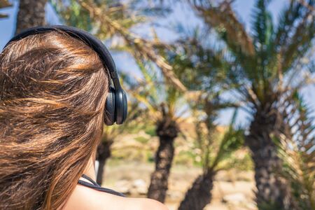 Back view on the girl in the headphones listening music  walks in the palm forest. Seychelles islandsの写真素材
