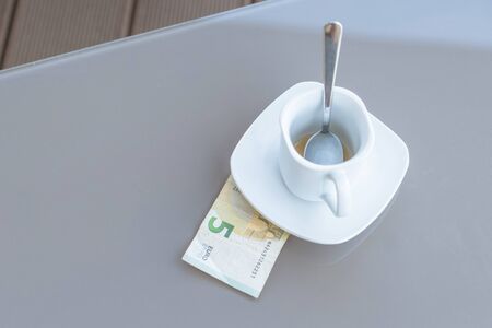 Five euros and empty cup of coffee on a glass table of outdoor cafe. Payment, tip.の写真素材