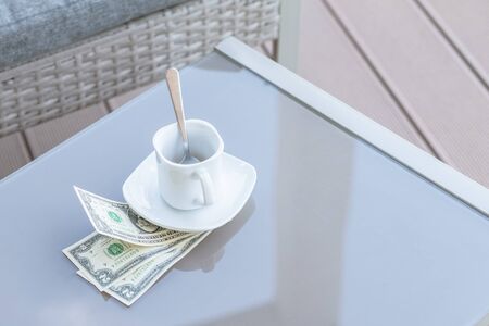 American dollars bill and empty cup of coffee on a glass table of outdoor cafe. Payment, tip.の写真素材