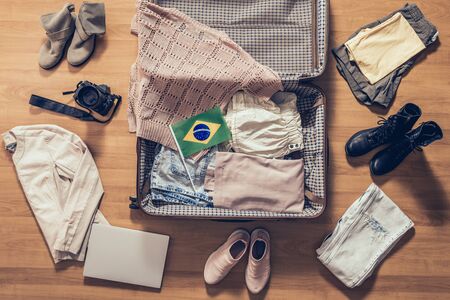 Woman's clothes, laptop, camera and flag of Brazil  lying on the parquet floor near and in the open suitcase. Travel conceptの写真素材