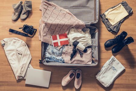 Woman's clothes, laptop, camera and flag of Denmark lying on the parquet floor near and in the open suitcase. Travel conceptの写真素材