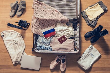Woman's clothes, laptop, camera, russian pasport and flag lying on the parquet floor near and in the open suitcase. Travel conceptの写真素材